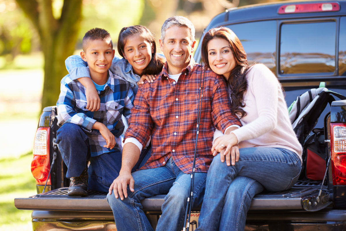 Family sitting in bed of pickup truck holiday camping